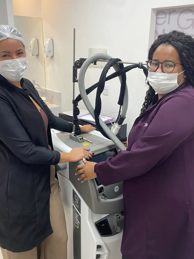 Profissionais da equipe GIO Jardim Suzana, de máscara e uniforme, ao lado de um equipamento de laser